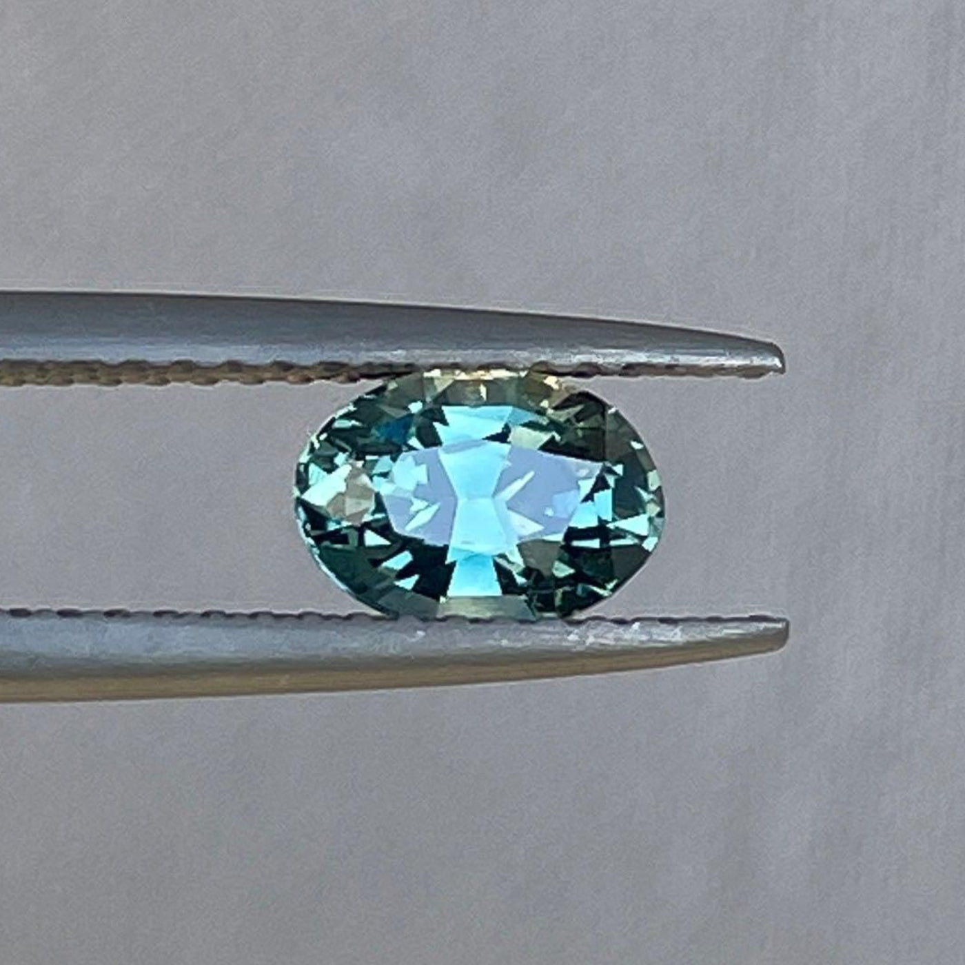 Saphir bleu sarcelle taille ovale de NASHGEMS, pierre précieuse naturelle de 1,00 carat pour bijoux personnalisés, présentée sur un fond blanc.