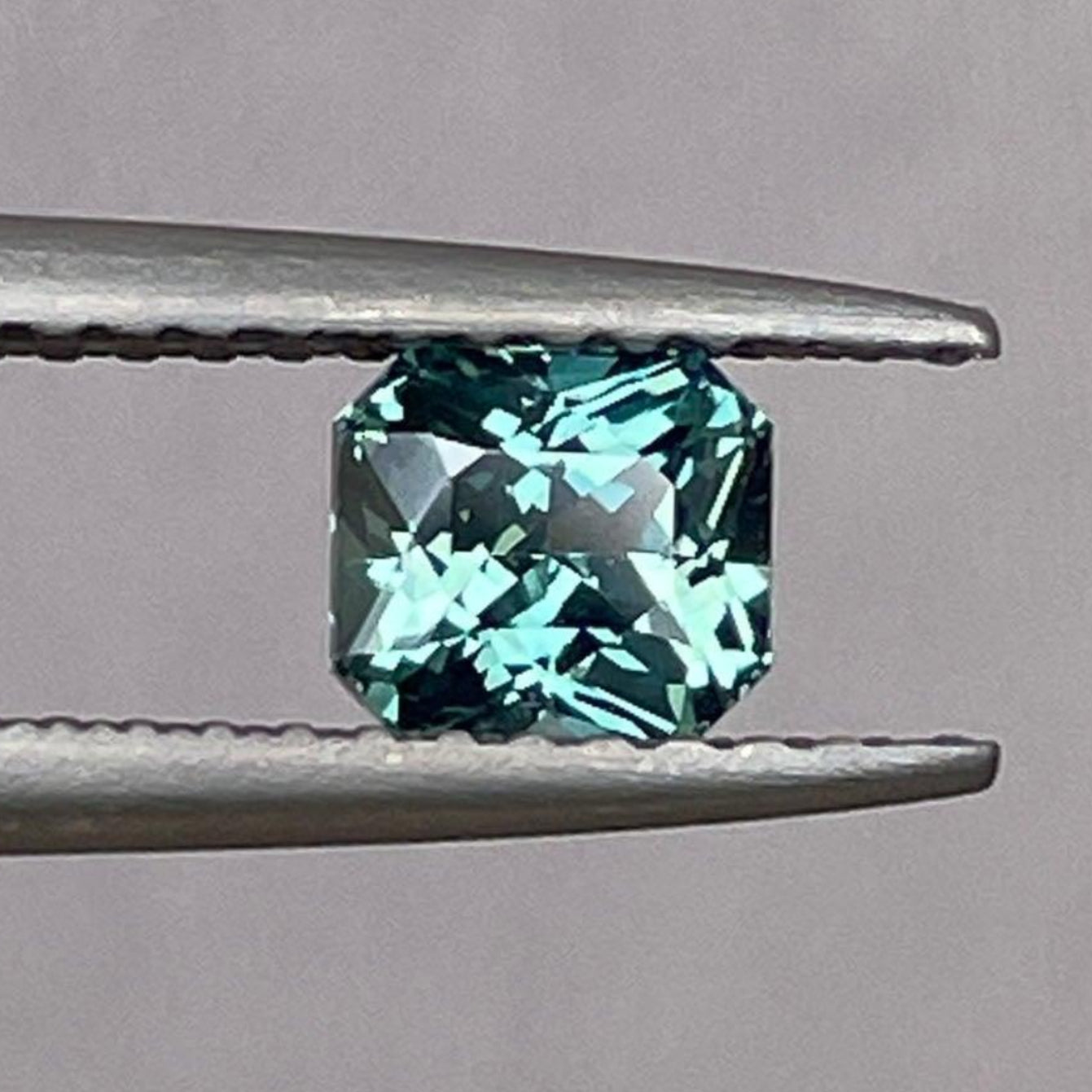 Loose teal sapphire gemstone with emerald cut, 0.79 carats, showcasing vibrant teal and blue-green hues, ideal for jewelry design.
