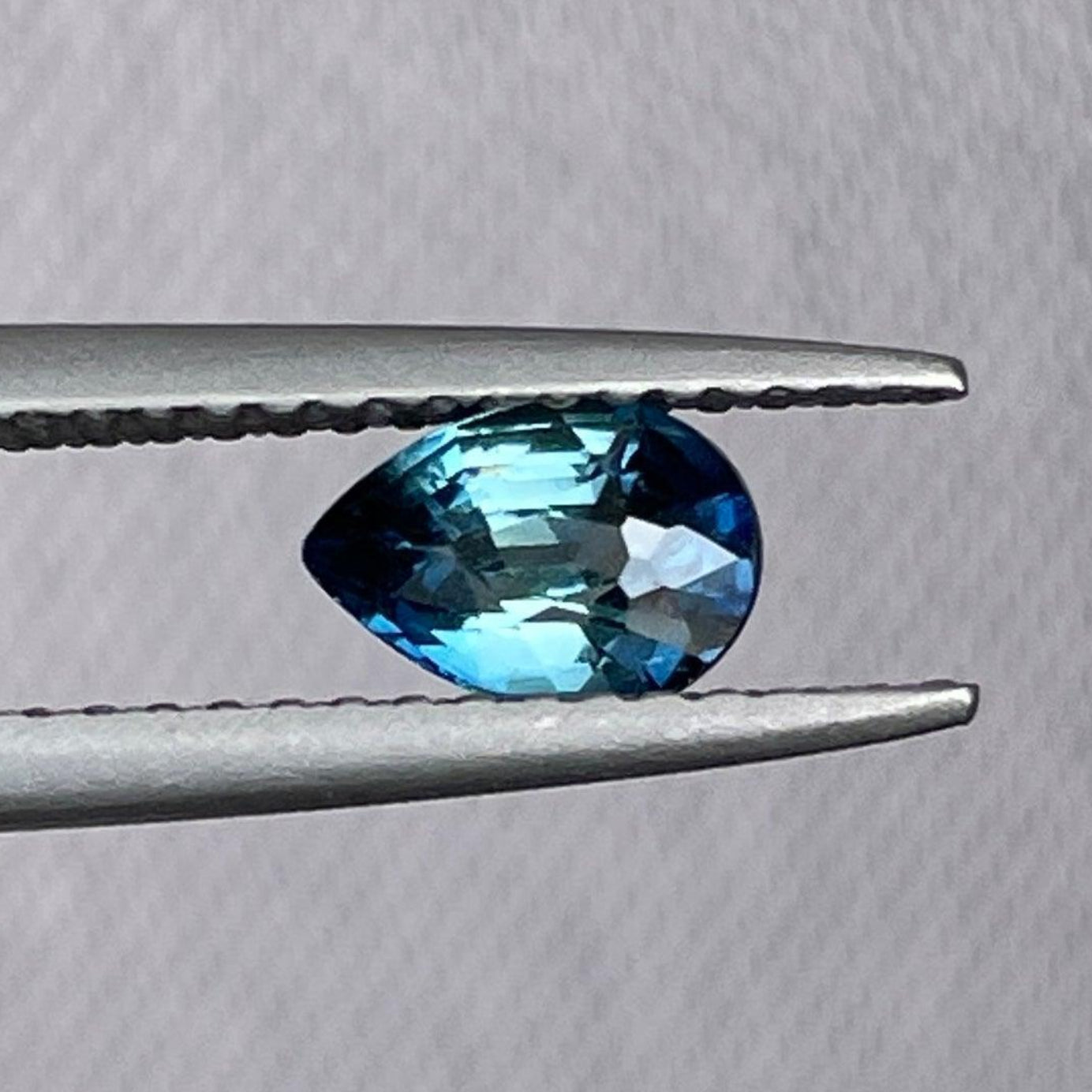 Pear cut teal sapphire gemstone from NASHGEMS, 0.71 carats, measuring 6.30 x 4.40 x 3.30mm, showing its vibrant color and clarity.