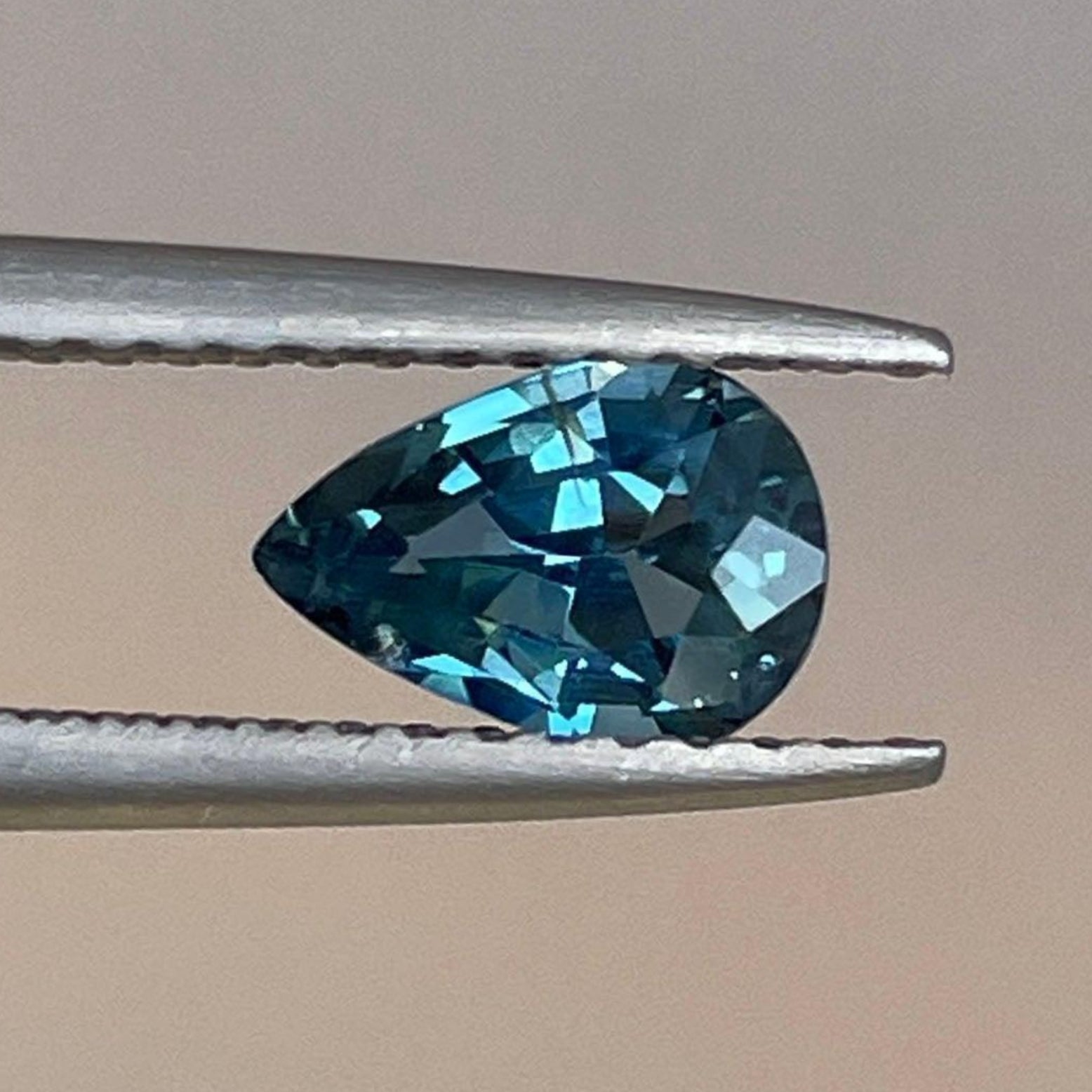 Teal sapphire pear-shaped gemstone, 0.87 carats, from NASHGEMS, showcasing its vibrant teal color and polished cut.