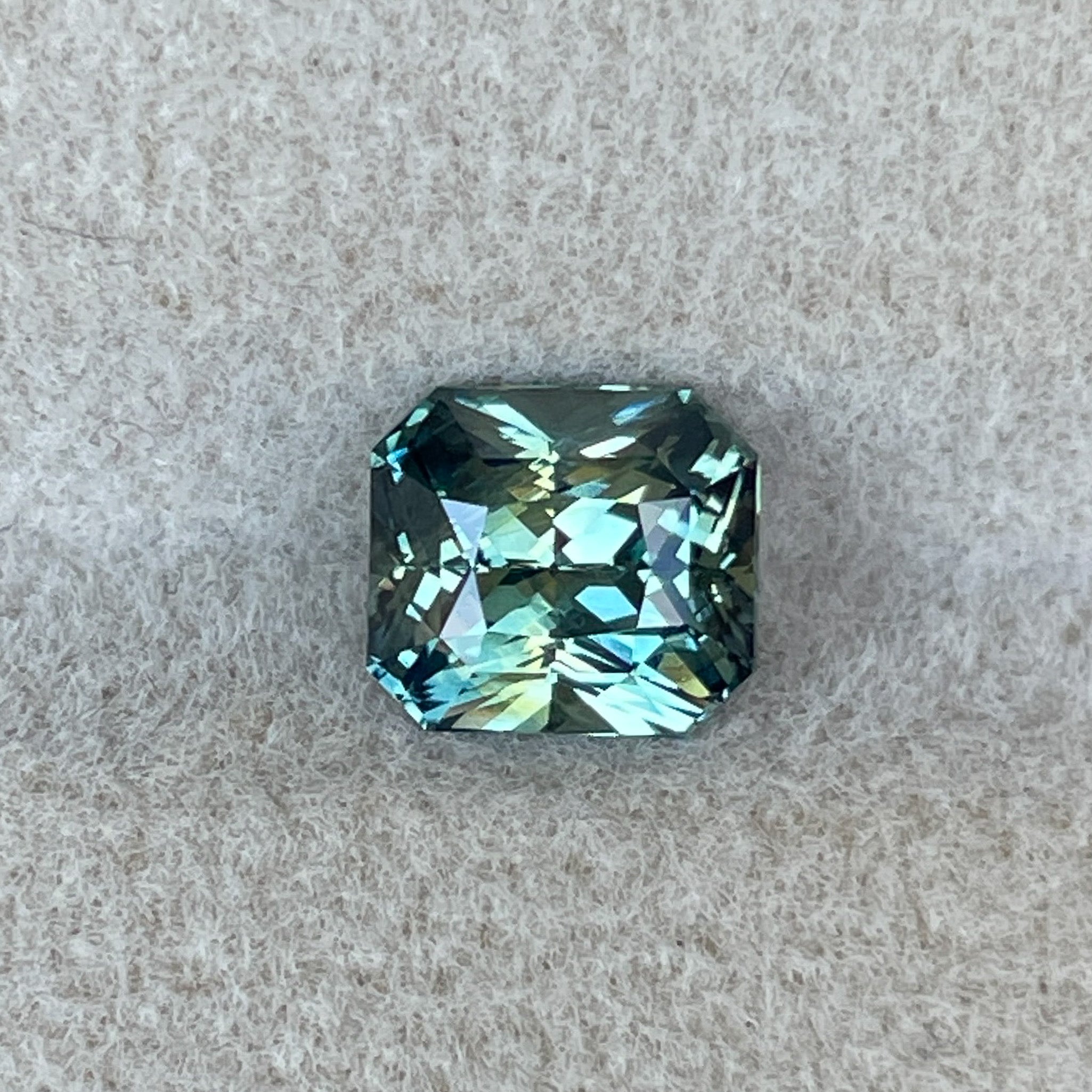Natural teal sapphire loose stone, 1.65 Ct radiant cut by NASHGEMS, showcasing vibrant blue-green color for jewelry or engagement rings.