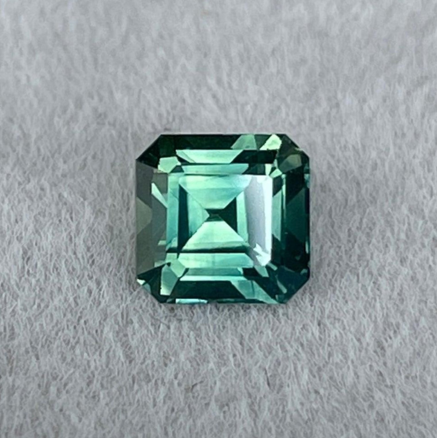 Pierre précieuse saphir vert naturel par NASHGEMS, saphir taille émeraude 0,96 ct aux teintes bleu sarcelle avec des nuances vert menthe foncé et clair ainsi que vert olive.