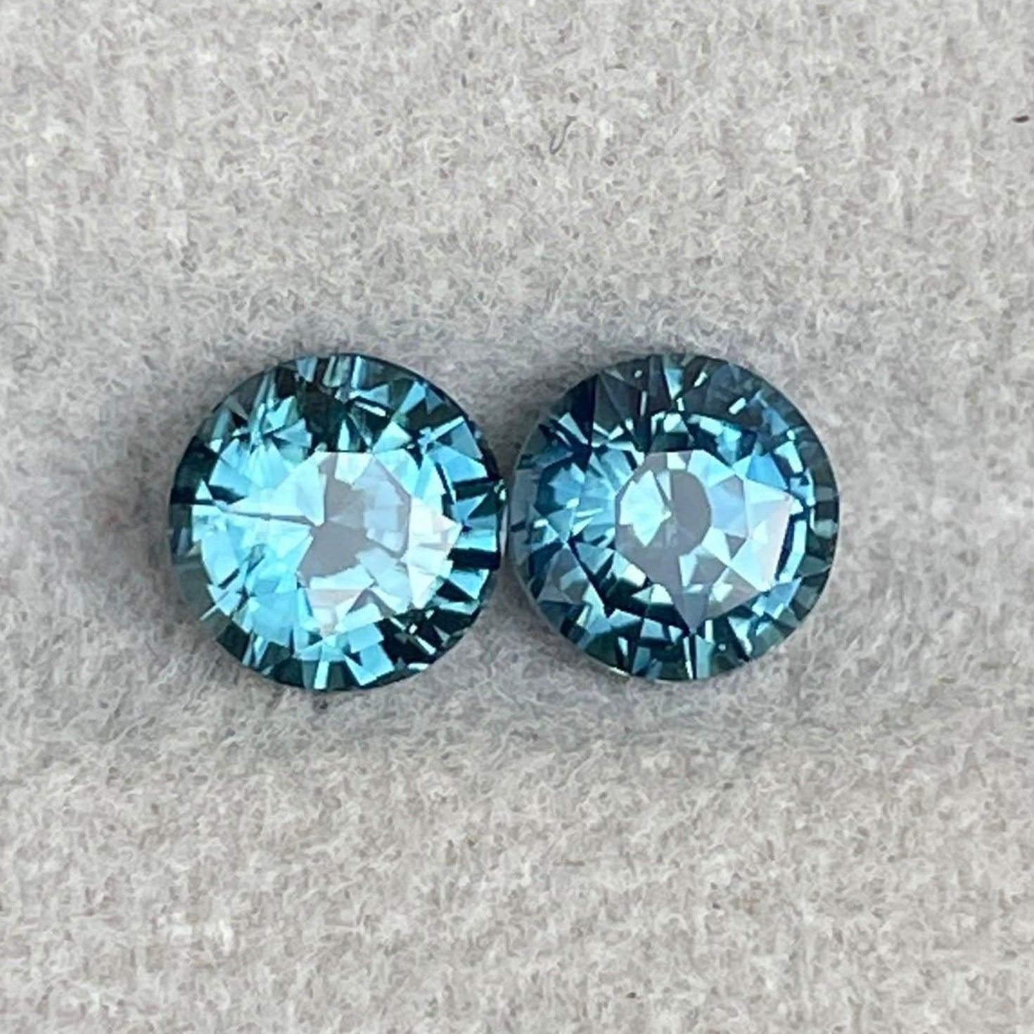 Pair of blue-green teal sapphire round cut gemstones from NASHGEMS, ideal for anniversary, engagement, or Mother's Day jewelry.