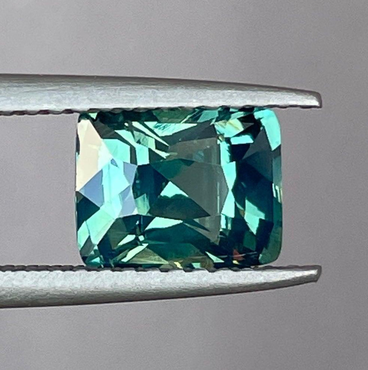 Teal sapphire cushion cut with stunning blue-green and greenish-blue hues, ideal for engagement rings by NASHGEMS.