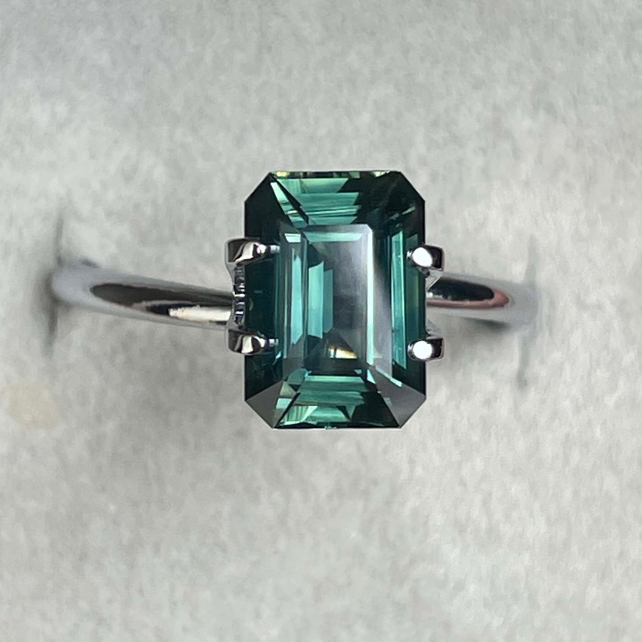 Natural green sapphire 3.03 ct emerald cut loose gemstone by NASHGEMS, showcasing vibrant teal color and faceted surface.