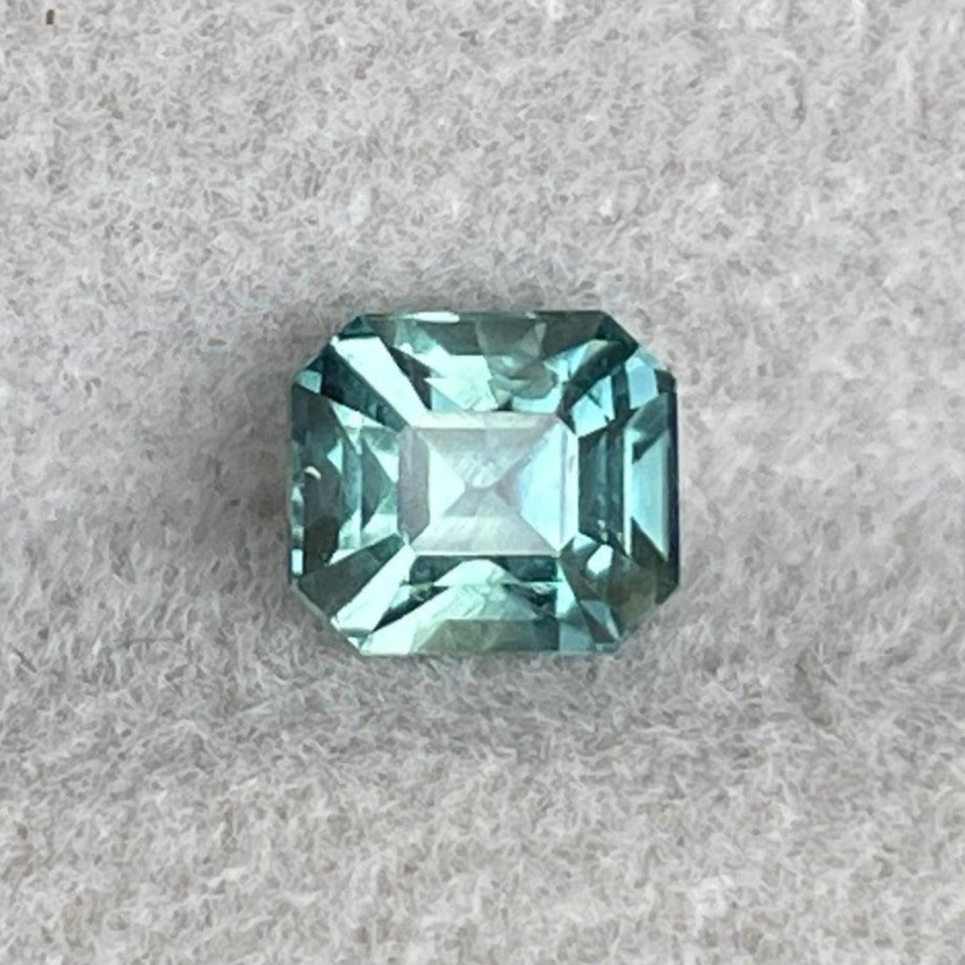 Saphir teal naturel chauffé taille Asscher de NASHGEMS, pesant 1,02 carat, présentant une couleur bleu-vert teal vif et une grande pureté.