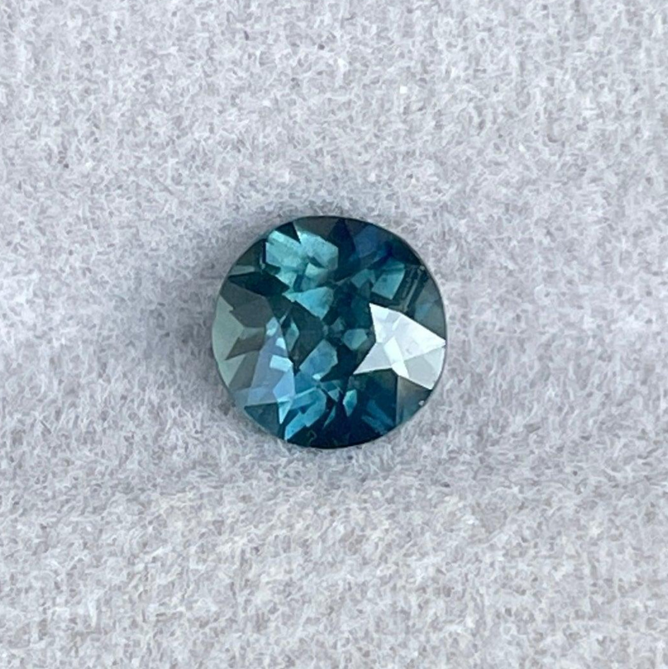 Blue green teal sapphire with round cut, 1.13 carats, set in an engagement ring, showcasing vibrant color and gemstone detail.
