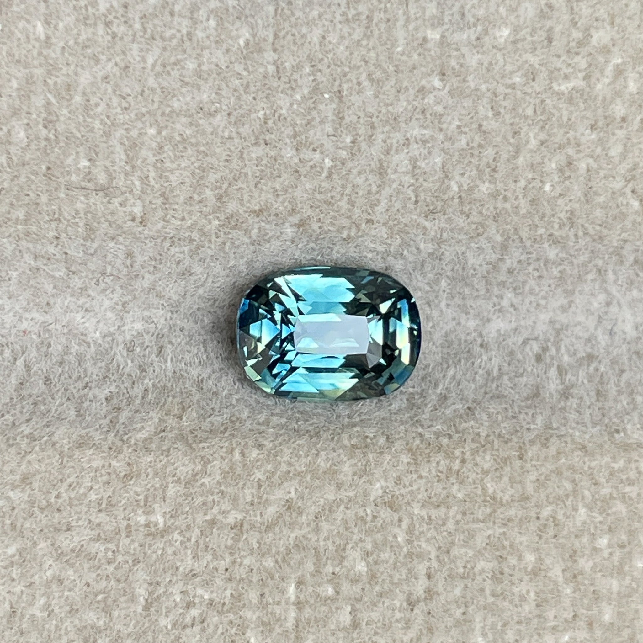 Natural teal sapphire 1.36 Ct cushion cut by NASHGEMS, showcasing vibrant blue-green hues, perfect for engagement or custom jewelry.